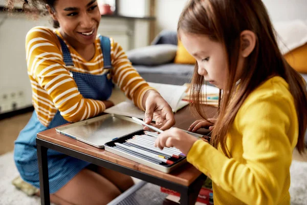 Caring. Close up of caucasian little girl spending time with african american baby sitter. Kid is drawing using colored pencils — Stock Photo, Image