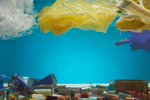 Primer plano de bolsas de plástico, baterías, desperdicio de alimentos y otros tipos de basura en el agua azul. Desastre ecológico y contaminación del concepto oceánico mundial — Foto de Stock