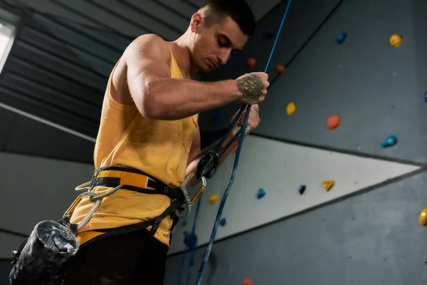 Homem esportivo jovem, alpinista segurando corda, pronto para o treinamento na parede de escalada artificial. Conceito de vida desportiva e escalada — Fotografia de Stock