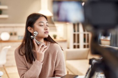 Cilt rutini. Genç bayan blogcu, güzellik blogu için video kaydederken yüzüne yüz silindiri ile masaj yapıyor. Yüz gerdirme, yaşlanma karşıtı tedavi konsepti