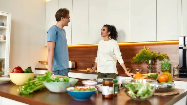 Pareja feliz, vegetarianos hablando mientras van a preparar comida saludable, sandwhich, ensalada en la cocina juntos. Vegetarianismo, comida saludable, concepto de dieta — Foto de Stock