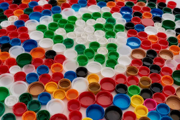 Close up of collage with colorful plastic bottle caps and recycling sign on white background. Reuse of waste concept. — Stock Photo, Image