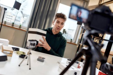 Genç erkek teknoloji blogcusu video blogu kaydediyor ya da yeni kamera lenslerinin ve diğer cihazların video günlüklerini ev stüdyosunda açıyor. Bloglama, Evden Çalışma kavramı