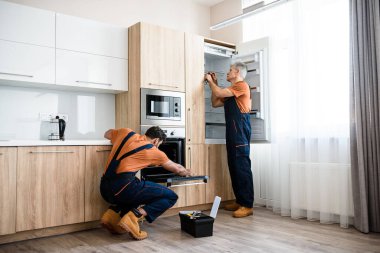 Güvenli ve uygun fiyatlı tamiratlar. İki tamirci, üniformalı işçiler mutfağa mobilya ve teçhizat yerleştiriyorlar. Kapalı alanda tornavida kullanıyorlar. Mobilya onarımı ve montaj konsepti