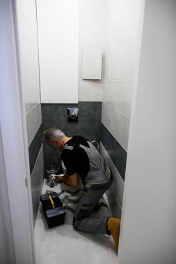 Üniformalı profesyonel tesisatçı içeride anahtar kullanarak tuvalet tankını tamir ediyor. Onarım servisi kavramı