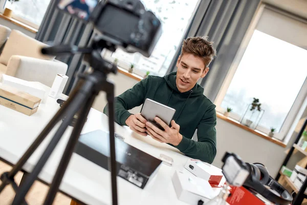 Le jeune blogueur technologique masculin enregistre un blog vidéo ou vlog sur une nouvelle tablette pc et d'autres gadgets au home studio. Blogging, concept de travail à domicile — Photo