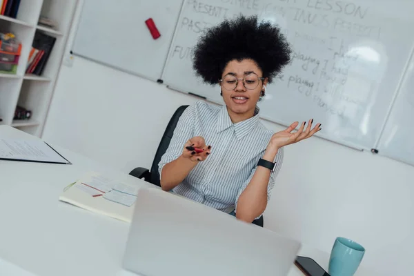 Angol óra. Fiatal vegyes fajú nő, női tanár ül a munkahelyén ellen whiteboard magyaráz valamit, miközben tanít angolul online — Stock Fotó