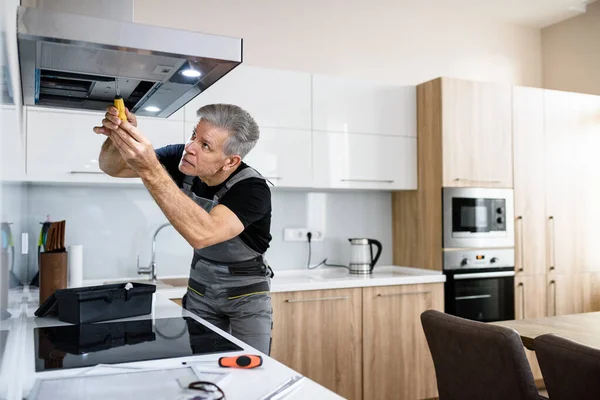 Rendi la tua vita più facile. Riparatore invecchiato in uniforme di lavoro, fissaggio rotto ventilatore dell'estrattore della cucina con cacciavite. Concetto di servizio riparazione — Foto Stock