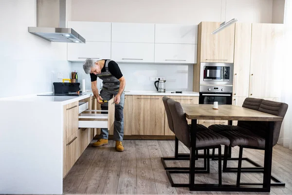 Plan complet du réparateur âgé en uniforme de travail, la fixation de l'armoire de cuisine à l'aide d'un tournevis. Concept de service de réparation — Photo