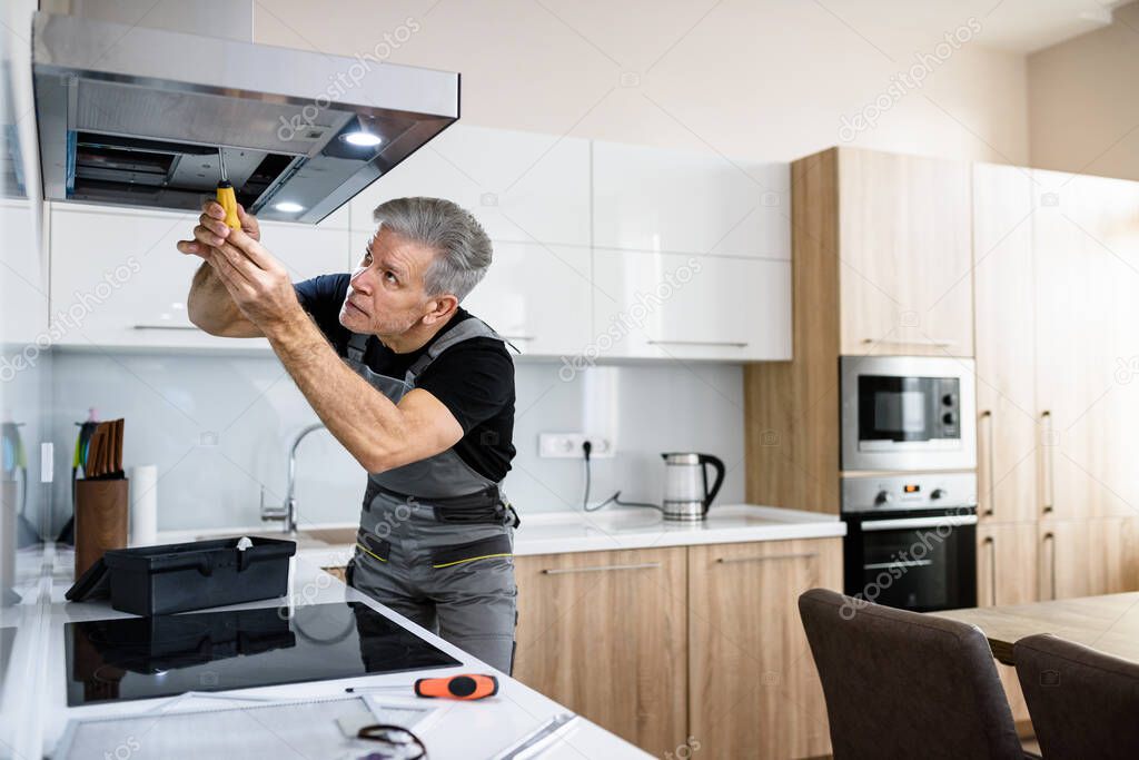 Make your life easier. Aged repairman in uniform working, fixing broken kitchen extractor fan using screwdriver. Repair service concept