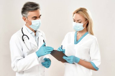 Tıbbi üniforma giyen ve koruyucu maskeler takan iki erkek ve kadın doktor laboratuvar testini tartışıyor, gri arka planda duruyorlar.