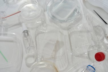 Kullanılmış plastik şişeler, kaplar, çatallar, kaşıklar, yumurta ambalajları, beyaz arka planda kapaklar