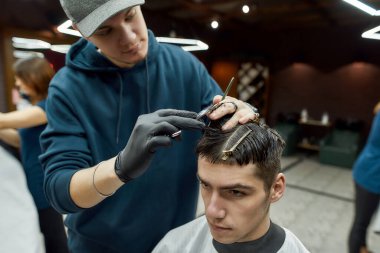 Profesyonel erkek berber berber koltuğunda oturan yakışıklı bir genç için yeni moda saç kesimi yapıyor. Berbere ya da güzellik salonuna gelen bir adam.