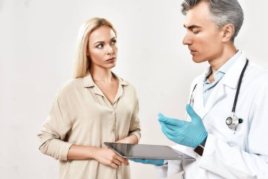 Teşhisi açıklıyorum. Tıbbi üniformalı profesyonel erkek doktor dijital tablet kullanıyor ve genç kadın hasta ile konuşuyor.