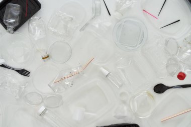 Kullanılmış plastik şişeler, kaplar, çatallar, kaşıklar, yumurta ambalajları, beyaz arka planda kapaklar
