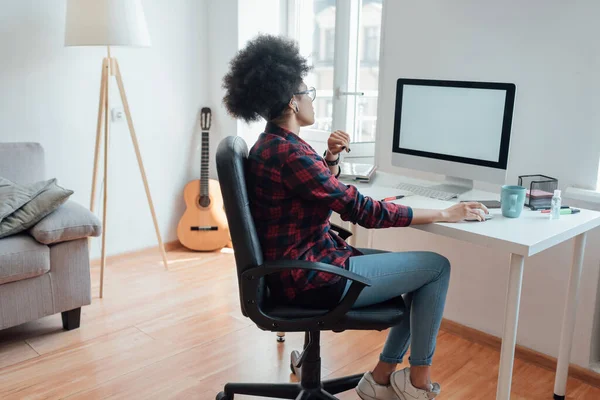 Un lieu de travail confortable. Vue latérale de la femme afro-américaine regardant l'écran d'ordinateur tout en travaillant ou en apprenant en ligne de la maison — Photo