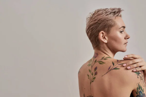 Sensualité. Portrait de beauté d'une jeune femme tatouée à moitié nue avec une peau parfaite regardant loin isolé sur fond gris — Photo