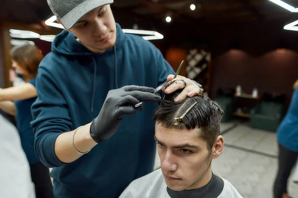 Profesyonel erkek berber berber koltuğunda oturan yakışıklı bir genç için yeni moda saç kesimi yapıyor. Berbere ya da güzellik salonuna gelen bir adam. — Stok fotoğraf