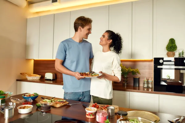 Egyél rendesen. Boldog pár, vegetáriánusok együtt készítik a reggelit a konyhában. Fiatal férfi és nő egészséges ételeket, szendvicseket készít. Vegarianizmus, egészséges ételek, étrend, maradj otthon koncepció — Stock Fotó
