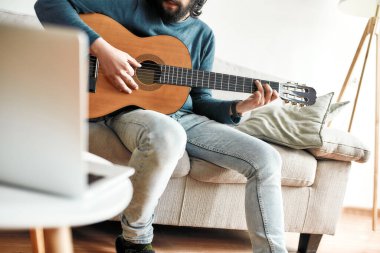 İnternetten ders. Evde oturup bilgisayar başında video dersi izlerken gitar çalan bir gencin görüntüsü.