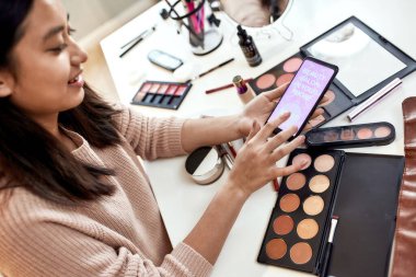 Güzel uygulama. Güzellik blogcusu kadın reklam uygulamasını kapat, akıllı telefon tut. Makyaj uzmanı Asyalı kız evde kozmetik ürünleri incelerken uygulama kullanıyor.