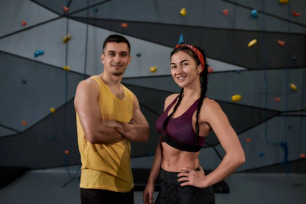 Ruh halini yükselt. Spor giyim sektöründe aktif bir genç adam ve kadın kameraya bakıyor, duvara tırmanıyor. Spor hayatı ve kaya tırmanışı kavramı — Stok fotoğraf