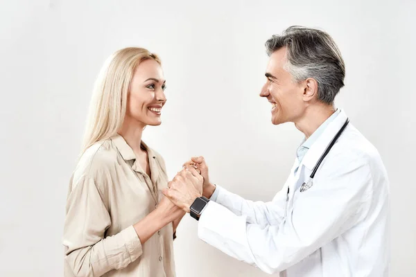 Ιατρική περίθαλψη και υποστήριξη. Χαμογελώντας ώριμος άντρας γιατρός με ιατρική στολή κρατώντας τα χέρια μιας νεαρής ευτυχισμένης γυναίκας ασθενούς — Φωτογραφία Αρχείου