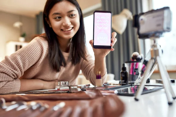 Κατεβάστε το. Beauty blogger γυναίκα γυρίσματα, διαφήμιση app στην κάμερα, κρατώντας smartphone. Makeup influencer ασιατική κορίτσι καταγραφή καλλυντικά αναθεώρηση του προϊόντος στο σπίτι — Φωτογραφία Αρχείου