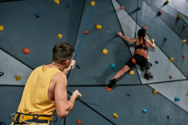 Instructeur masculin tenant la corde, tandis que la femme dans l'équipement de sécurité et la formation de harnais sur le mur d'escalade artificielle — Photo