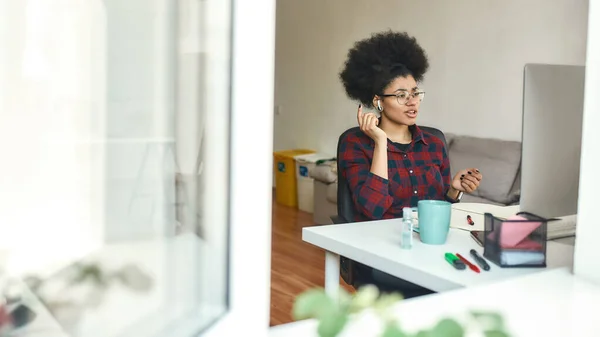 E-learning. Giovane studentessa afro-americana con cuffie wireless che studia lingua straniera online a casa. Vista dalla strada attraverso la finestra — Foto Stock