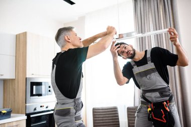 Biz mükemmeliz. İki elektrikçi, üniformalı işçiler elektrik lambası takıyor, mutfaktaki dairede ışık var. İnşaat dekorasyonu kavramı