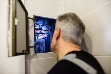 Yaşlı tesisatçı, üniformalı tamirci banyoda el feneri kullanarak boruları inceliyor. Onarım servisi kavramı