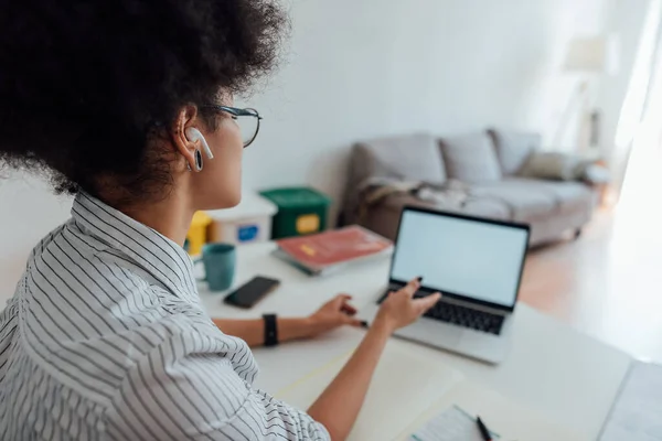 Vista posteriore della donna afro-americana che indossa cuffie wireless guardando la webcam e insegnando inglese online mentre lavora da casa — Foto Stock