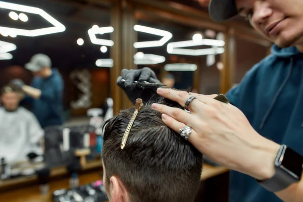 Taglio di capelli alla moda. Foto ravvicinata di un barbiere professionista di sesso maschile che lavora con forbici e pettine, realizzando un taglio di capelli per il cliente. Uomo in visita dal barbiere — Foto Stock