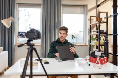 Genç erkek teknoloji blogcusu video blogu veya video blogu kaydediyor. Yeni tablet bilgisayar ve diğer cihazlar hakkında. Bloglama, Evden Çalışma kavramı