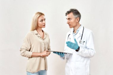 Doktor ve hasta. Tıbbi üniformalı profesyonel erkek doktor dijital tablet kullanıyor ve genç bayan hastalarla konuşuyor.