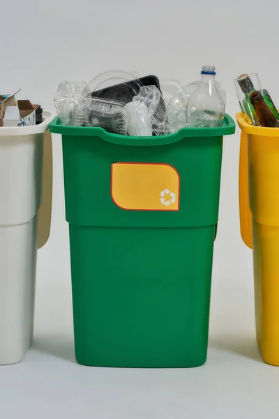 Papelera de reciclaje verde con cartel de reciclaje en ella llena de basura de pie en una fila con otros contenedores aislados sobre fondo blanco. Concepto de separación de residuos —  Fotos de Stock