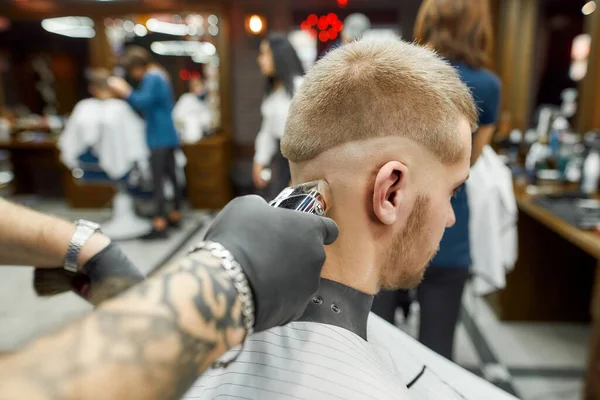 Genç bir adamın berber dükkanını ziyaret edip yeni moda saç tıraşı olduğu yakın plan bir fotoğraf. Berber saç makasıyla çalışıyor, arkadan bakıyor. Kafaya odaklan. — Stok fotoğraf