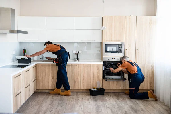 Tamir et. İki tamirci, üniformalı işçiler mutfağa mobilya ve teçhizat yerleştiriyorlar. Kapalı alanda tornavida kullanıyorlar. Mobilya onarımı ve montaj konsepti — Stok fotoğraf