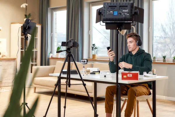 Joven blogger de tecnología masculina grabando video blog o vlog sobre nuevos auriculares y otros dispositivos en el estudio en casa. Blogging, Trabajo desde el hogar concepto —  Fotos de Stock