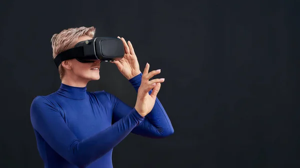 Mujer con pelo corto en cuello alto azul con auriculares de realidad virtual, gafas vr aisladas sobre fondo oscuro —  Fotos de Stock