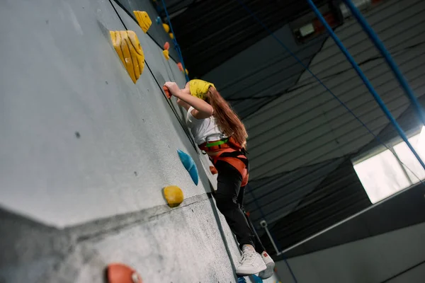 Chica que usa equipo de seguridad y entrenamiento de arnés, subiendo a la pared artificial en el interior. Concepto de formación de Bouldering —  Fotos de Stock