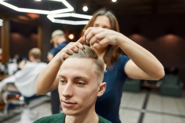 Çalışma süreci. Berber dükkanında müşteriye hizmet eden profesyonel berber kız ya da kadın kuaför, jöleli ya da balmumlu genç adamın saçını şekillendiriyor.