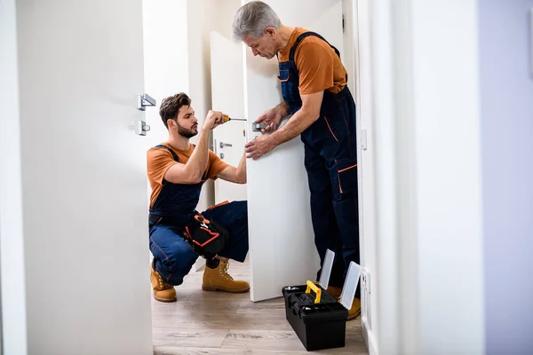 İki çilingir, tamirci, üniformalı işçiler tornavida kullanarak kapı kilidiyle uğraşırken tam boy çekim. Onarım, kapı kilidi servisi konsepti — Stok fotoğraf