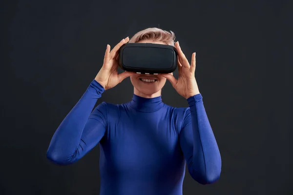 Mujer excitada con pelo corto en cuello alto azul con auriculares de realidad virtual, gafas vr aisladas sobre fondo oscuro —  Fotos de Stock