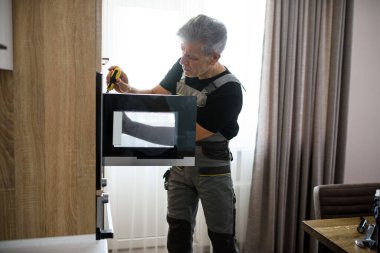 Tamir ettiriyorum. Üniformalı yaşlı bir tamirci tornavidayla mutfakta bozuk mikrodalgayı tamir ediyor. Onarım servisi kavramı