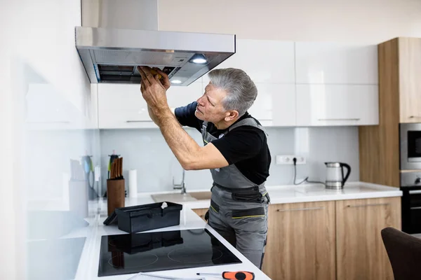 Arreglar su problema tecnológico. Reparador de edad en uniforme de trabajo, la fijación de ventilador de extractor de cocina roto utilizando destornillador. Servicio de reparación concepto — Foto de Stock