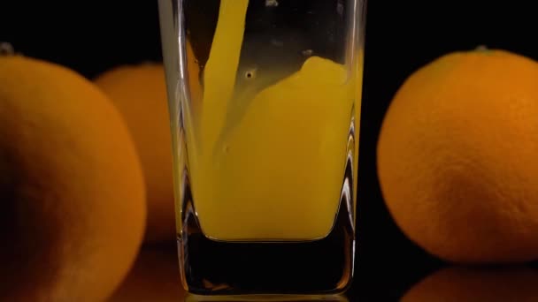 Voller Früchte. Super-Zeitlupenaufnahme des Einfüllens von Orangensaft in ein transparentes Glas und zwei Orangen vor schwarzem Hintergrund. Aus nächster Nähe. Gesundes Getränk, Vitamine, Fruchtkonzept — Stockvideo