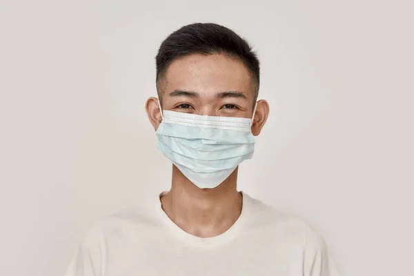 Máscara puesta. Retrato de un joven asiático con máscara médica, sonriendo a la cámara aislada sobre fondo blanco. Salud, prevención, concepto de seguridad — Foto de Stock
