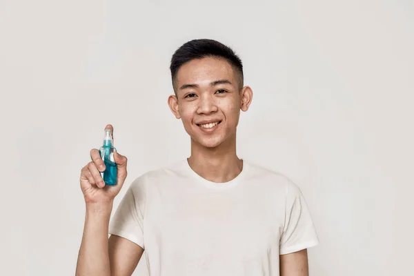För din säkerhet. Porträtt av ung asiatisk man med rent rakat ansikte ler mot kameran, hålla handen desinfektionsmedel isolerad över vit bakgrund. Hälso- och sjukvård — Stockfoto